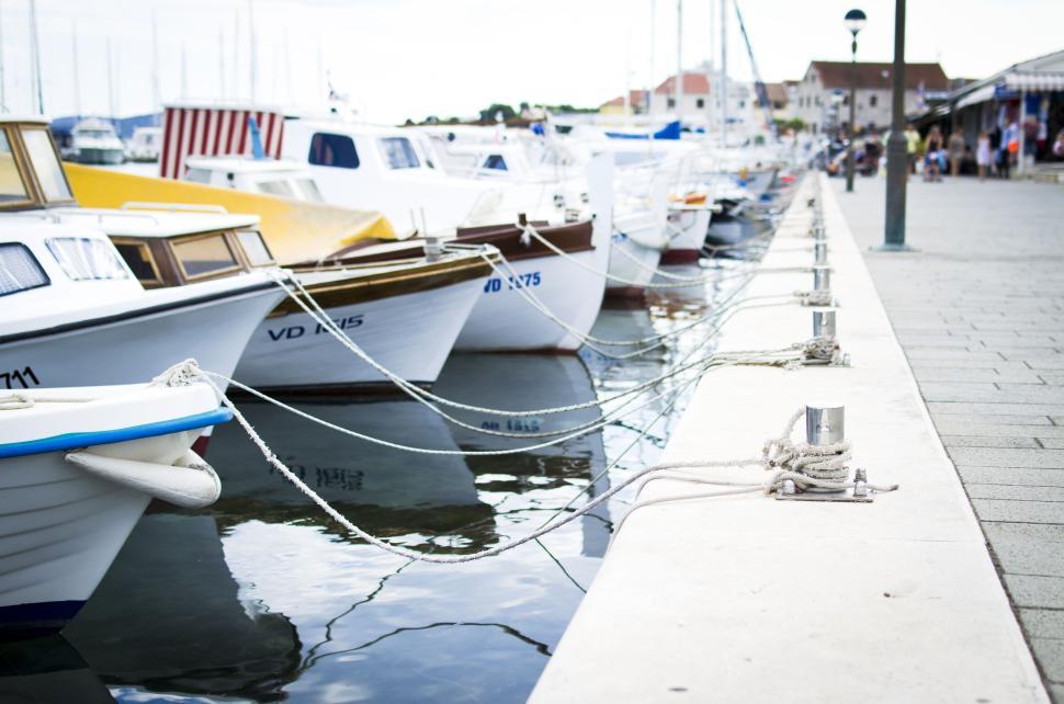 Free Image of Boats docked at a marina with buildings and people in the background 