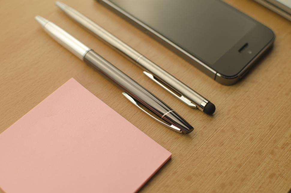 Free Image of Work essentials on wooden desk with smartphone and pens 