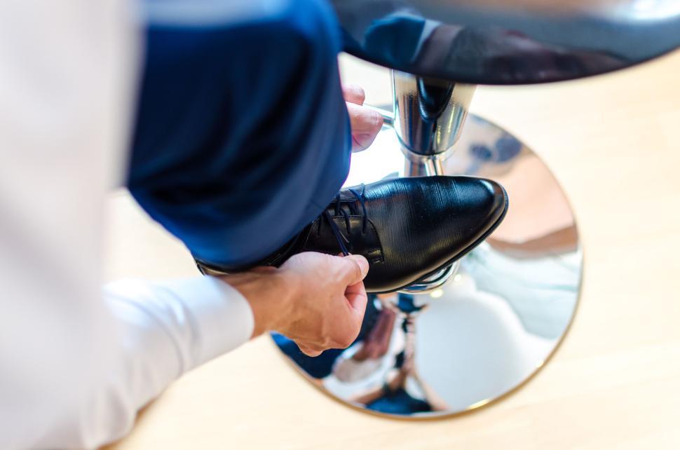 Free Image of Man tying formal shoes while seated on a shiny surface chair. 