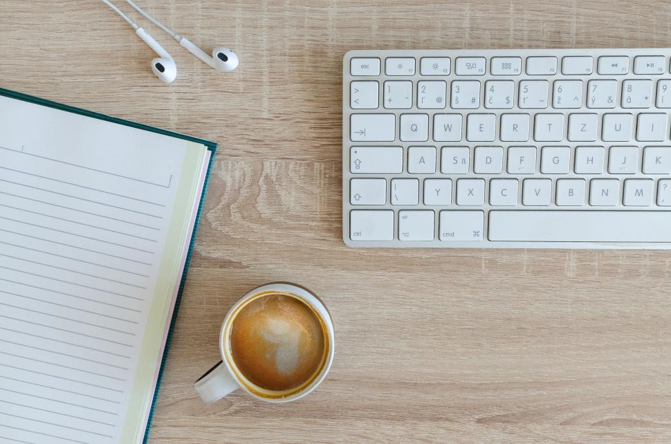 Free Image of Workspace with notebook, keyboard, coffee, and earphones on desk. 
