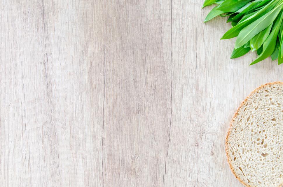 Free Image of Wooden surface with a slice of bread and green leafy garnish. 