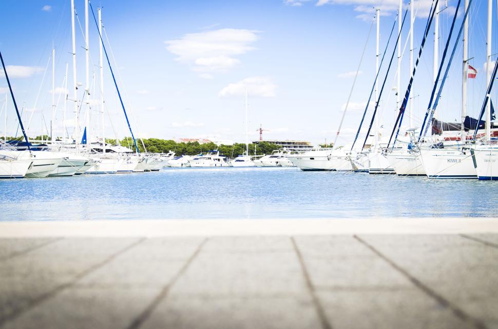 Free Image of Yachts on a harbor with clear blue sky and fluffy clouds above 