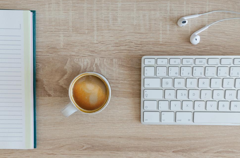 Free Image of Coffee, notebook, keyboard, and earphones arranged on wooden desk 