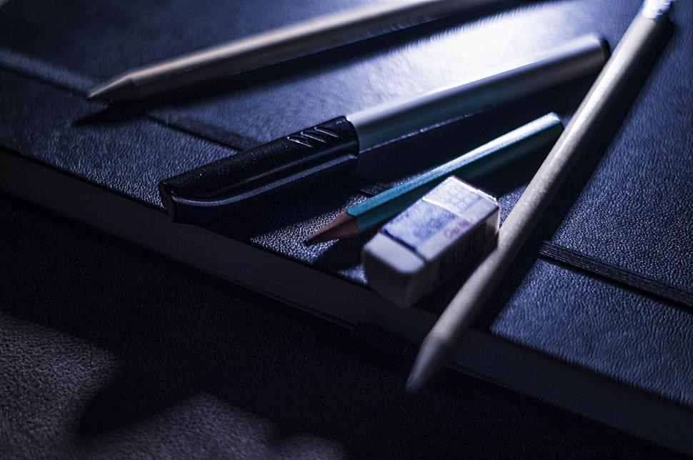 Free Image of Stationery items on a black notebook in dim lighting 