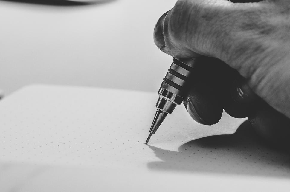 Free Image of Hand holding pen writing in notebook with a dotted page. 