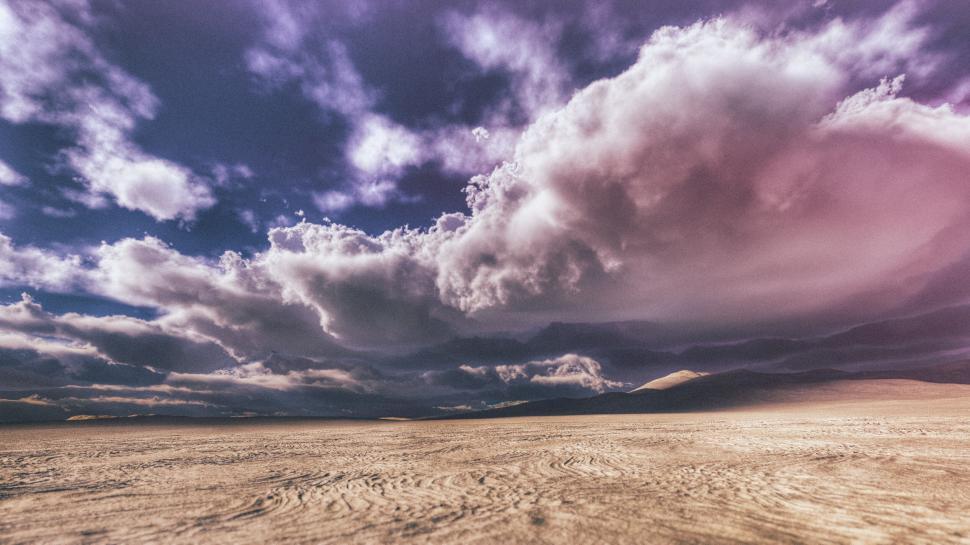 Free Image of Expansive desert landscape beneath a vivid sky filled with dramatic clouds 