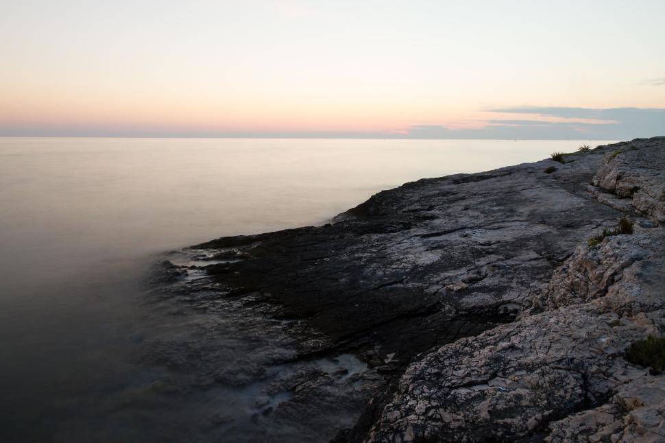 Free Image of Rocky shoreline meeting the calm sea during a tranquil evening. 