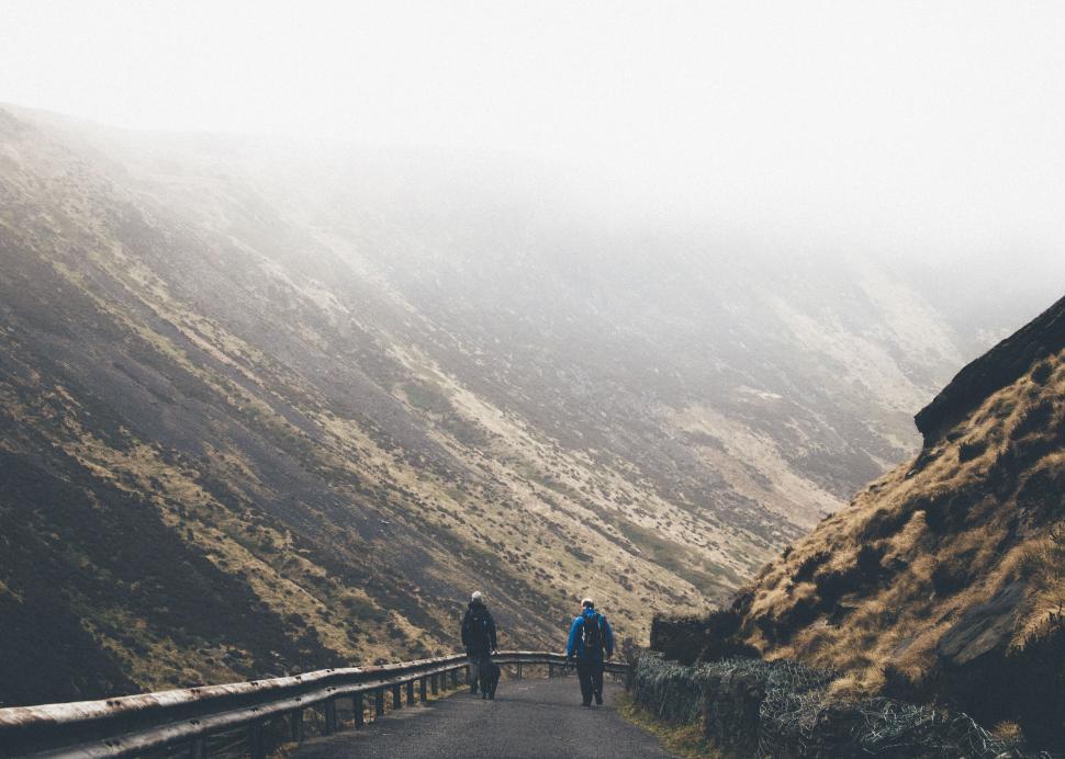 Free Image of People walking down a misty mountain road covered with grass. 