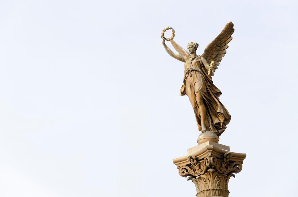 Free Image of Golden angel statue holding a wreath on an ornate pedestal in sunlight 