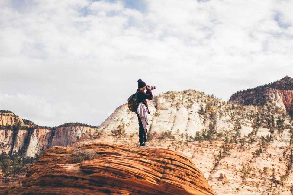 Free Image of Person atop a rocky hill capturing a photograph in a desert landscape 