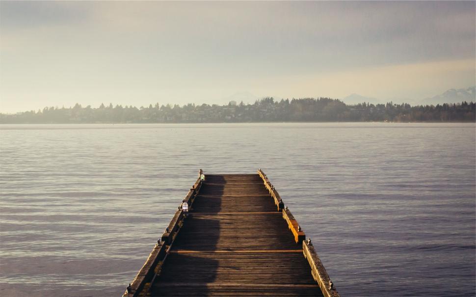 Free Image of Sunny dock leading out to a calm blue lake with distant mountains 