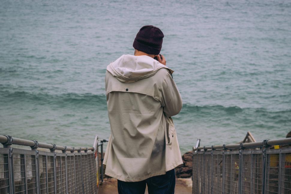 Free Image of Individual in beanie jacket looks at the calm sea from a stairway 
