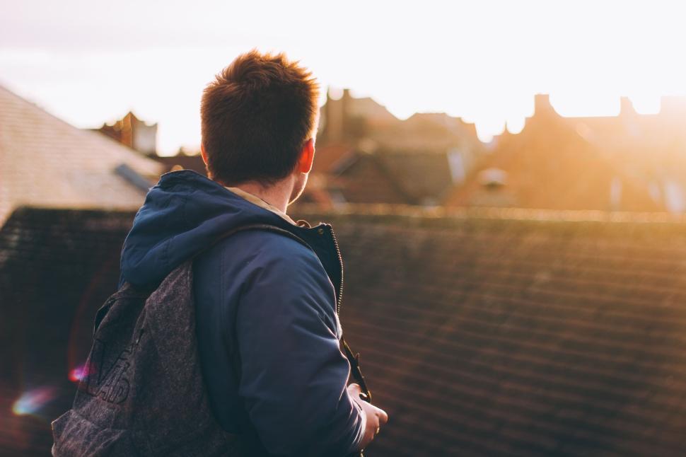Free Image of Kid wearing backpack, standing on a rooftop with sunset view. 