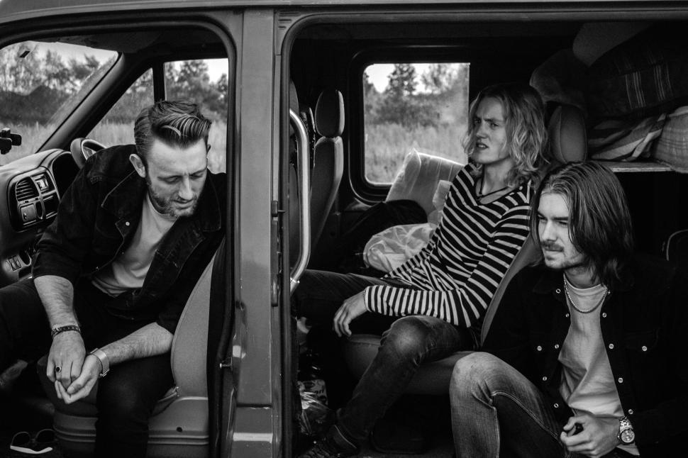 Free Image of Three friends sitting in a van, one looking out the window 