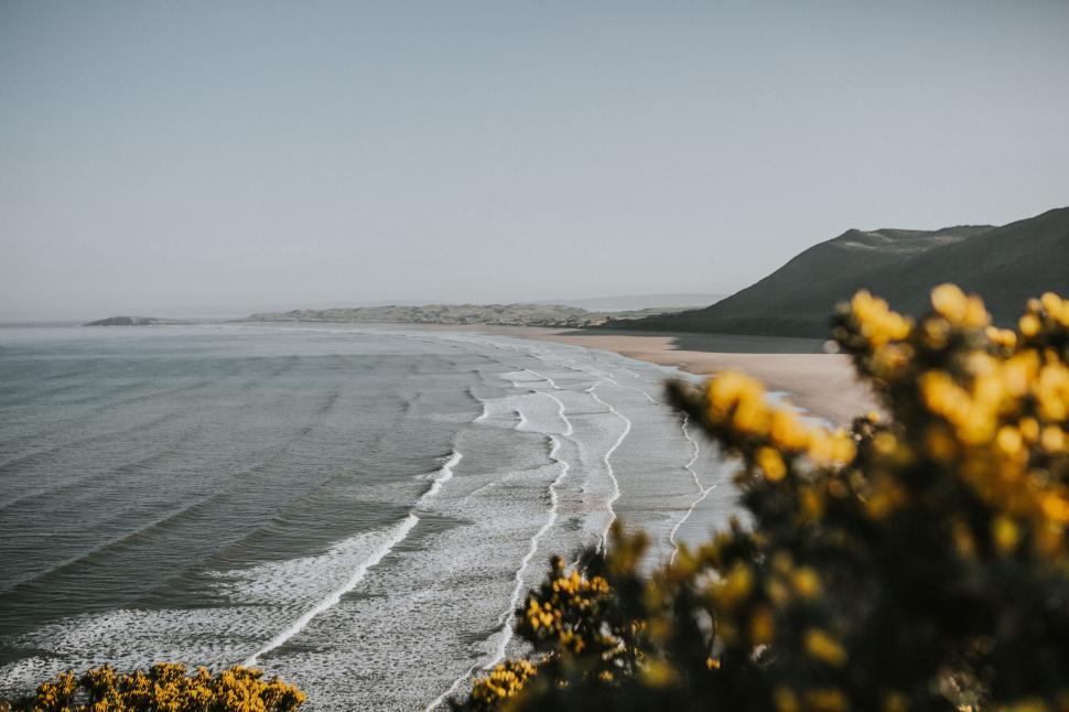 Free Image of Waves crashing on a broad beach with a scenic, hilly background. 