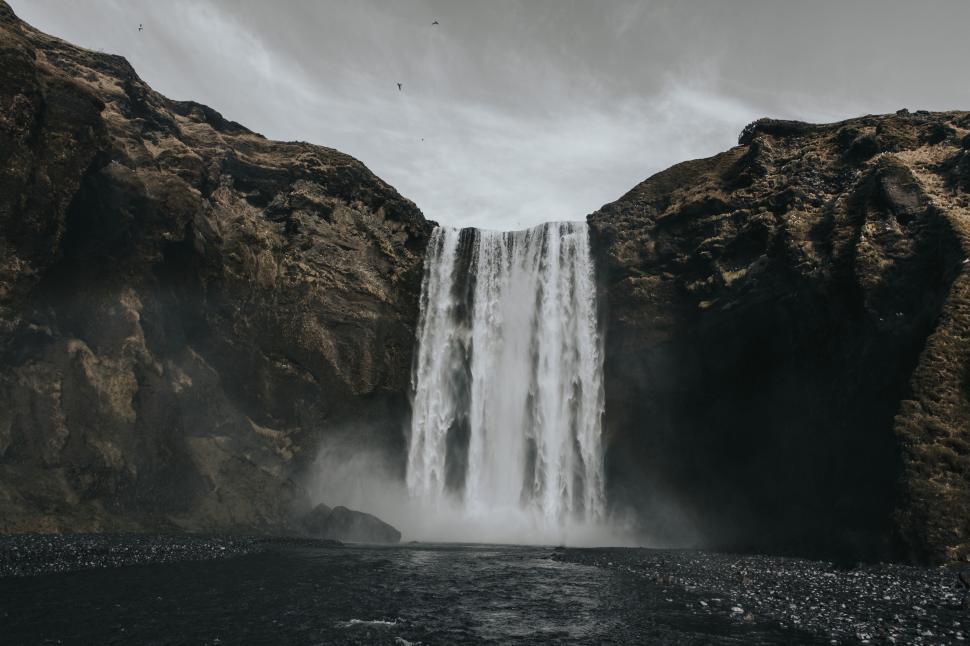 Free Image of Waterfall cascading down rocky cliffs into misty pool below. 