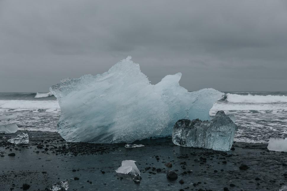 Free Image of Large iceberg washed ashore on black sand beach with crashing waves. 