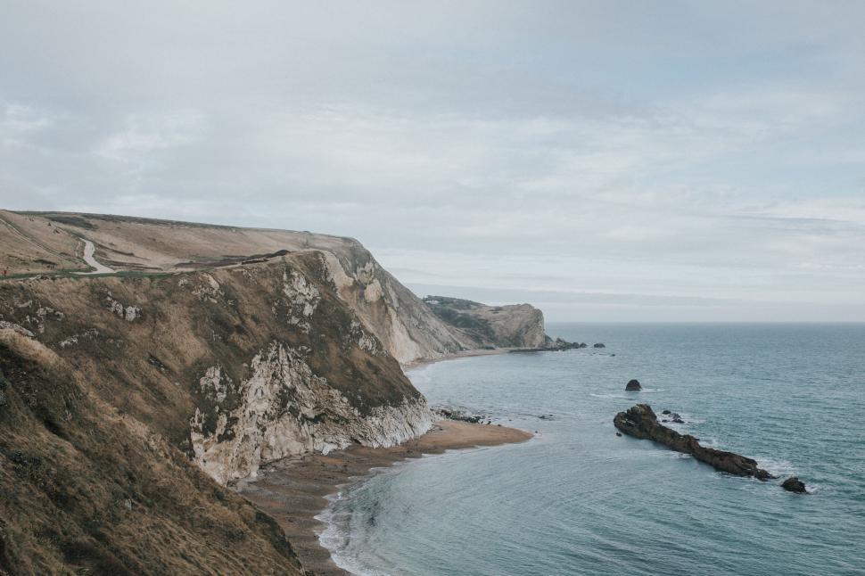 Free Image of Coastal cliffside overlooking ocean with winding road in foreground 