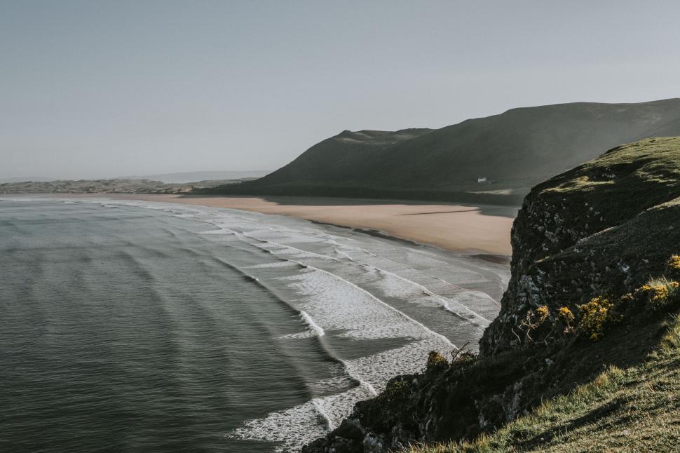 Free Image of Wide sandy beach with rolling waves and scenic coastal backdrop 
