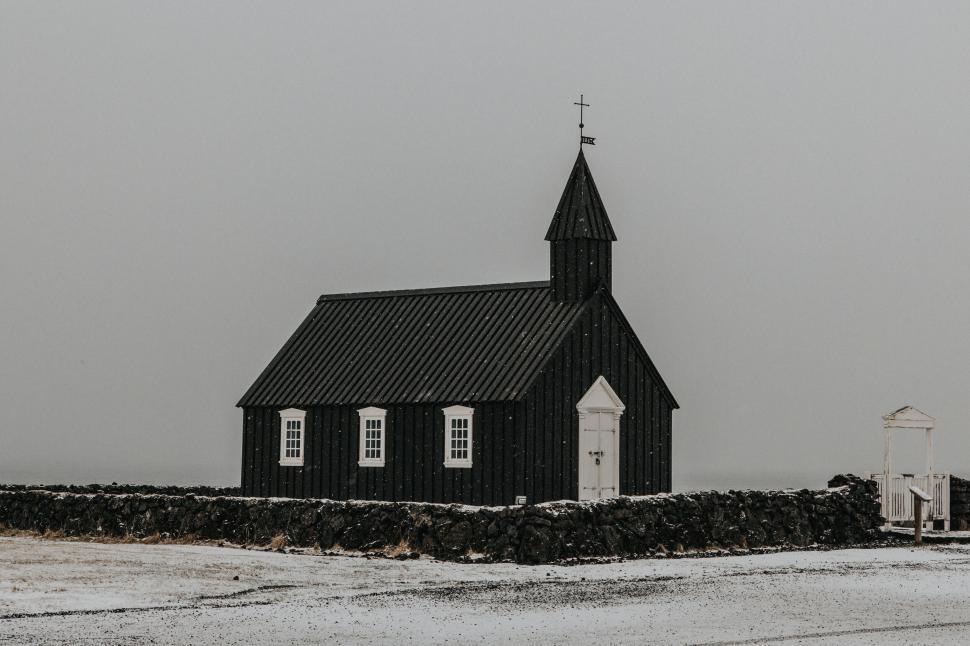 Free Image of Small, black wooden church on snowy landscape with overcast sky. 