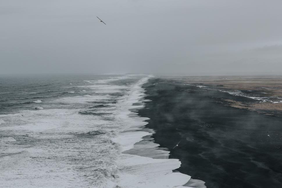 Free Image of Black sand beach with crashing waves and misty horizon view 
