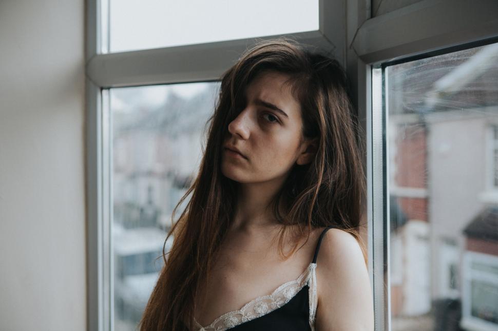 Free Image of A woman leaning against a window looking pensive 