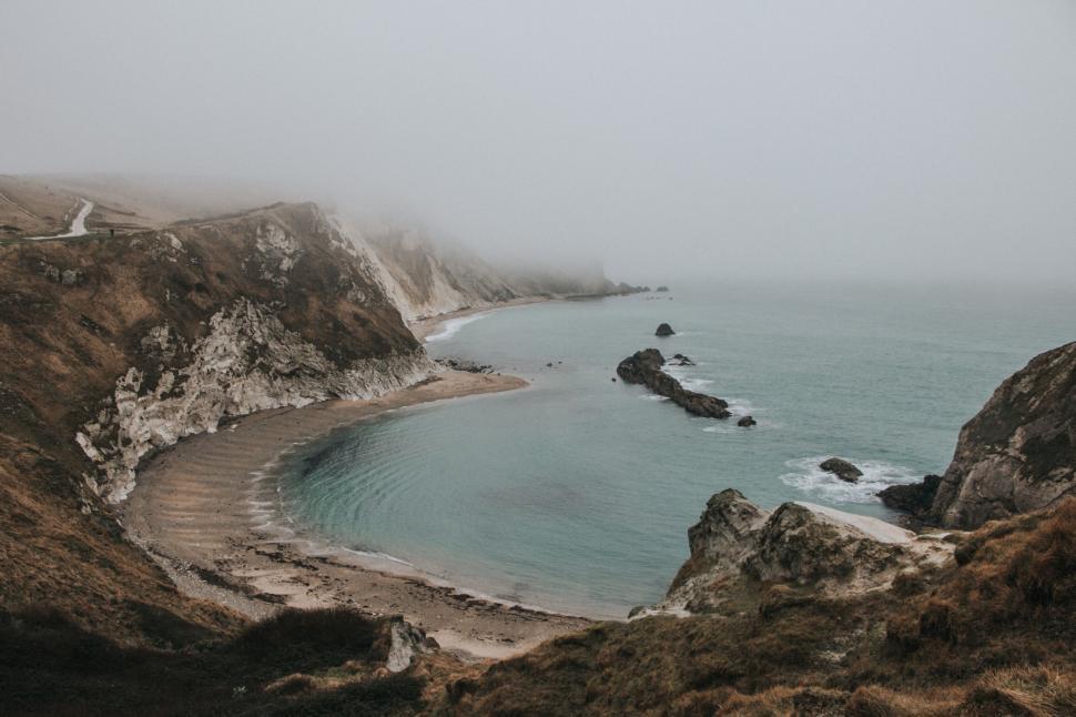 Free Image of Foggy coastal bay with smooth waves gently touching the shore. 