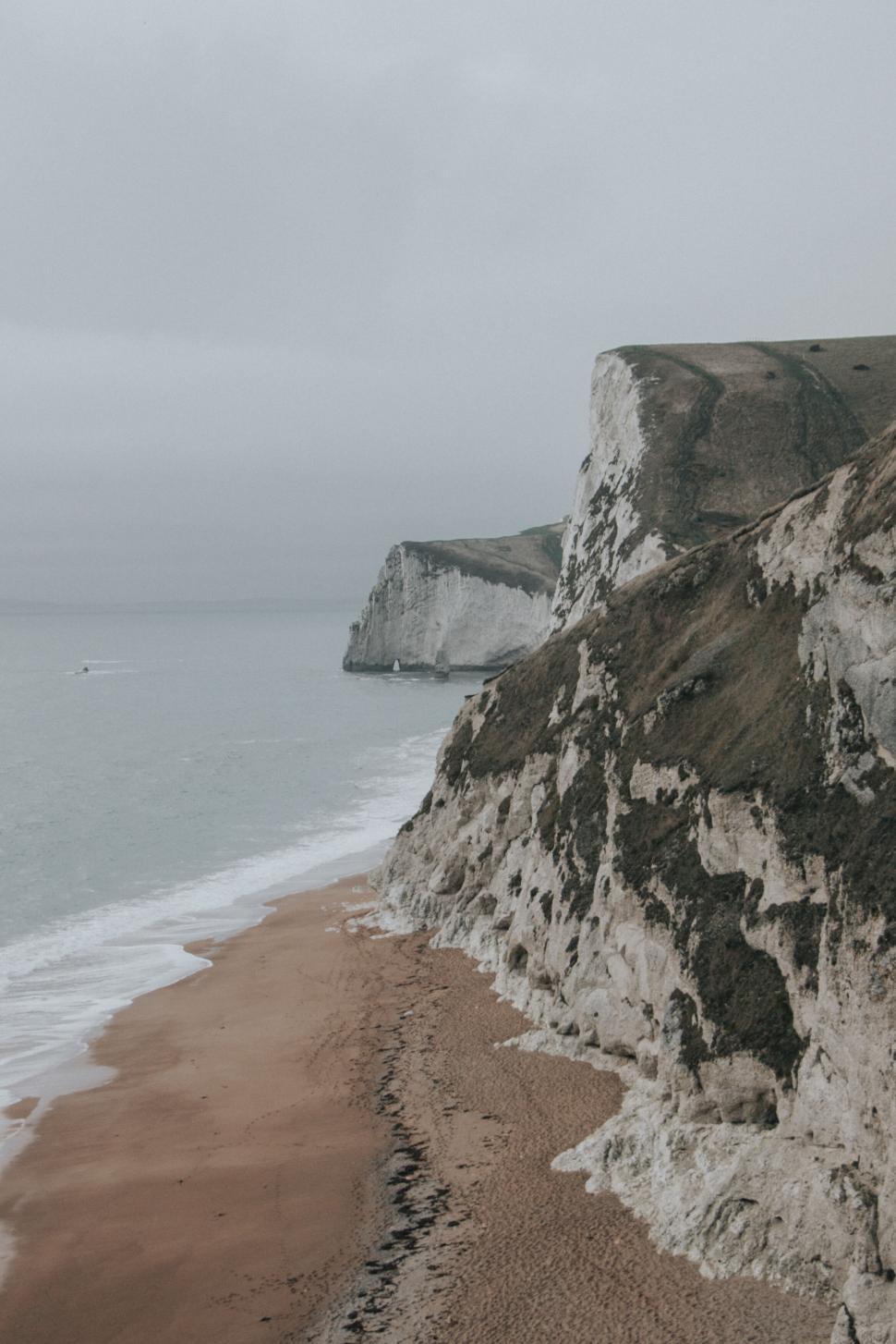 Free Image of Cliffs by the sea with sandy beach and overcast sky background. 