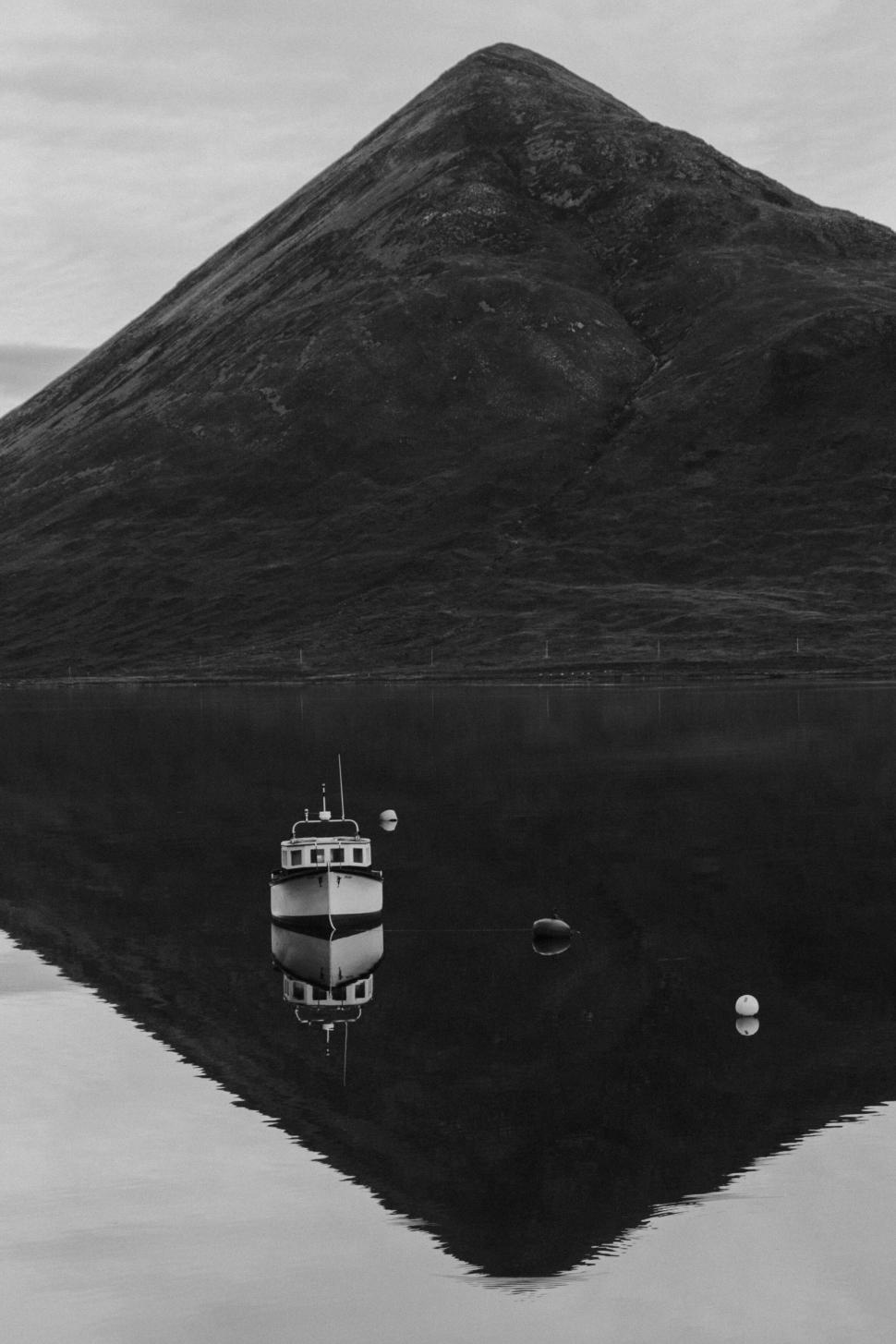 Free Image of Boat on still lake with mountain reflecting on water surface. 
