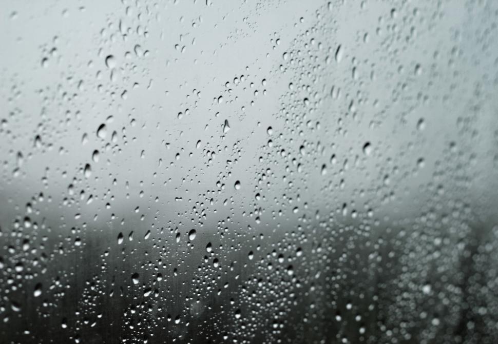 Free Image of Raindrops on a window with blurred rainy landscape in background. 