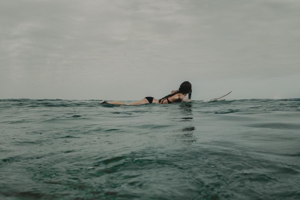 Free Image of Surfer laying on surfboard in the ocean under cloudy sky. 