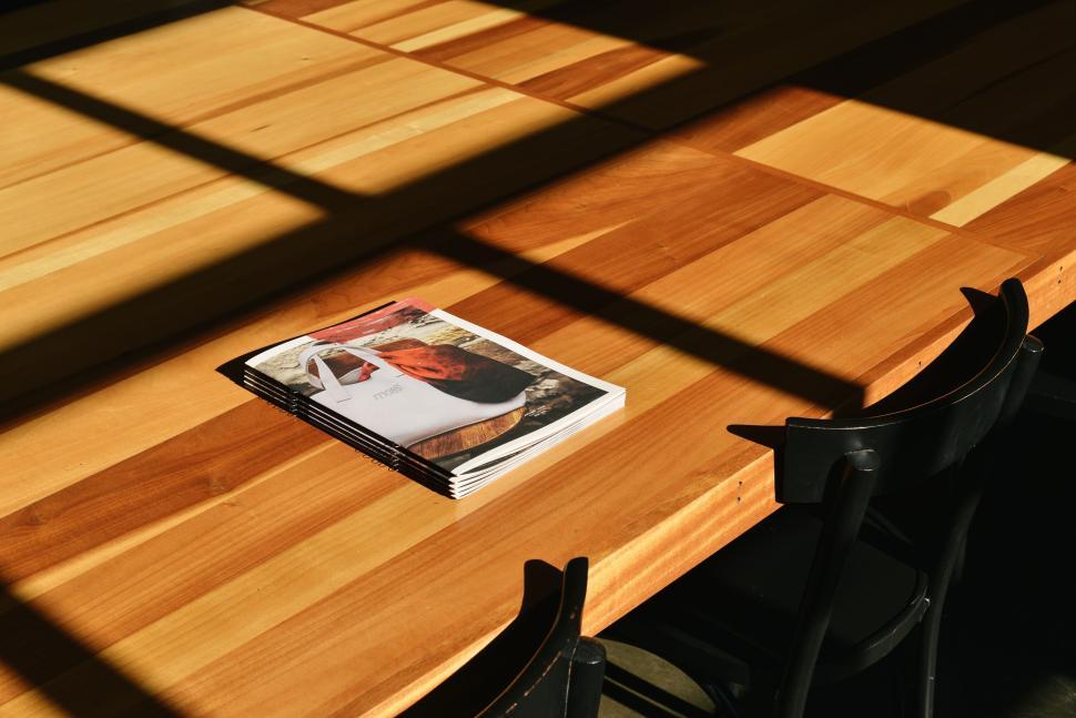 Free Image of Stack of magazines on a wooden table bathed in sunlight shadows 