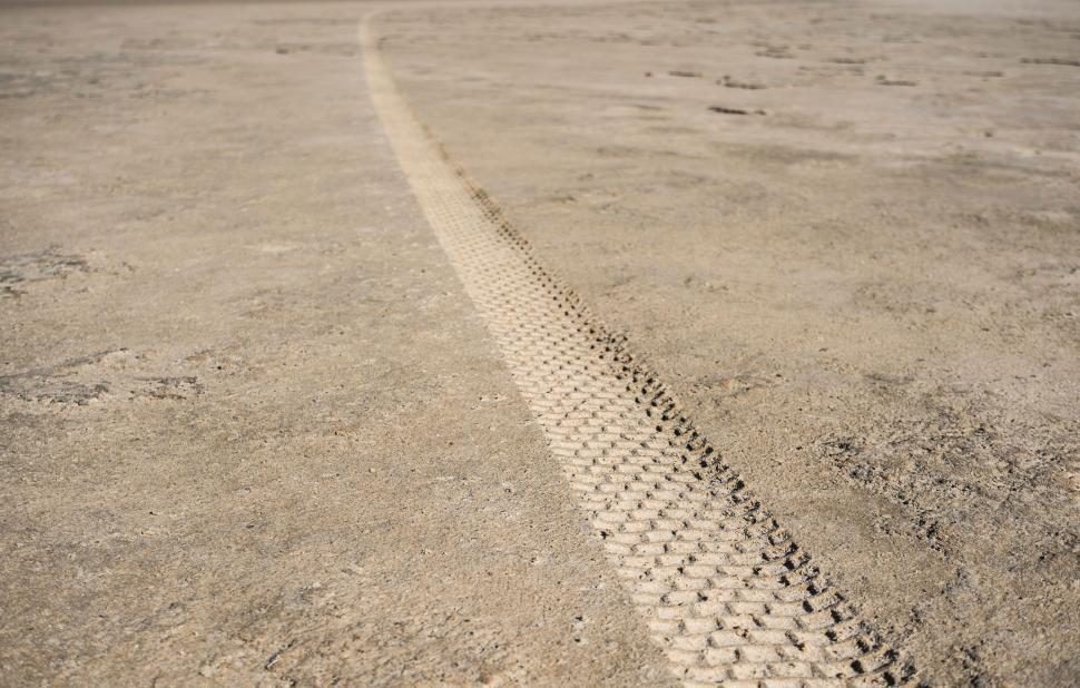 Free Image of Single tire track curving across a barren landscape of dry ground 