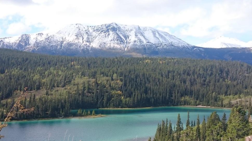 Free Image of Snow-capped mountains overlooking a forest and clear blue lake. 