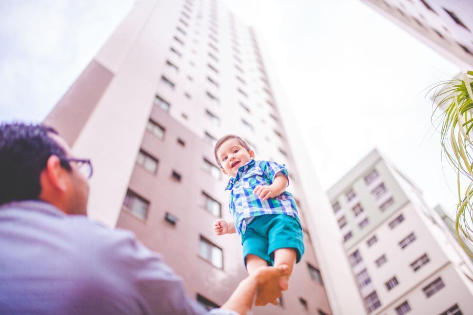 Free Image of Father lifting child in a courtyard surrounded by tall buildings 