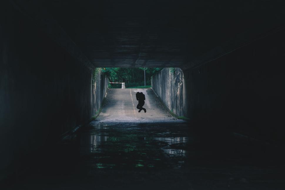 Free Image of Silhouette of person jumping in a dark tunnel with light ahead 