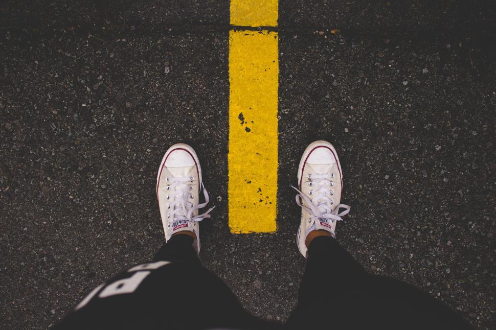 Free Image of Person in white shoes standing on asphalt with yellow line in middle 