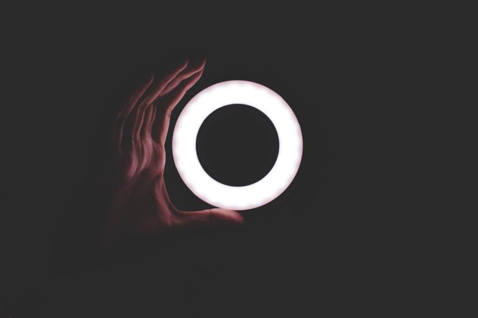 Free Image of Hand holding a bright circular light, dark background emphasizing glow 