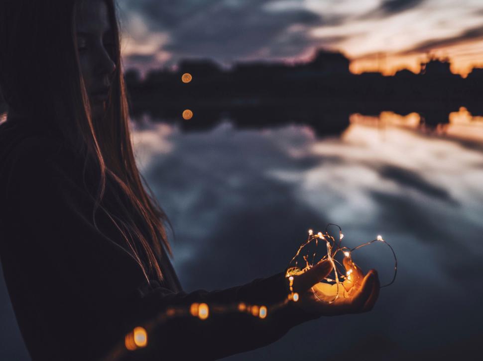 Free Image of Individual Embracing Fairy Lights by the Evening Water 
