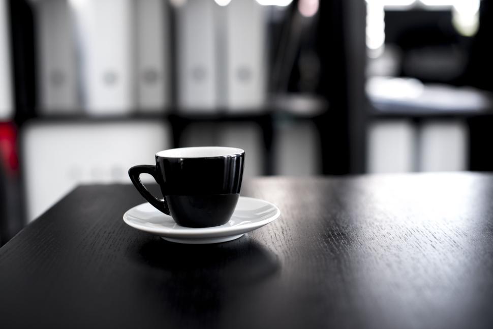 Free Image of Black coffee cup on a white platter against a blurred office background 