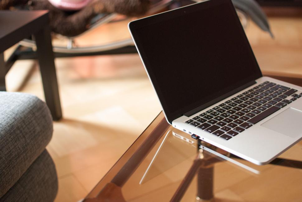 Free Image of A laptop sits on a glass table in a contemporary living space. 