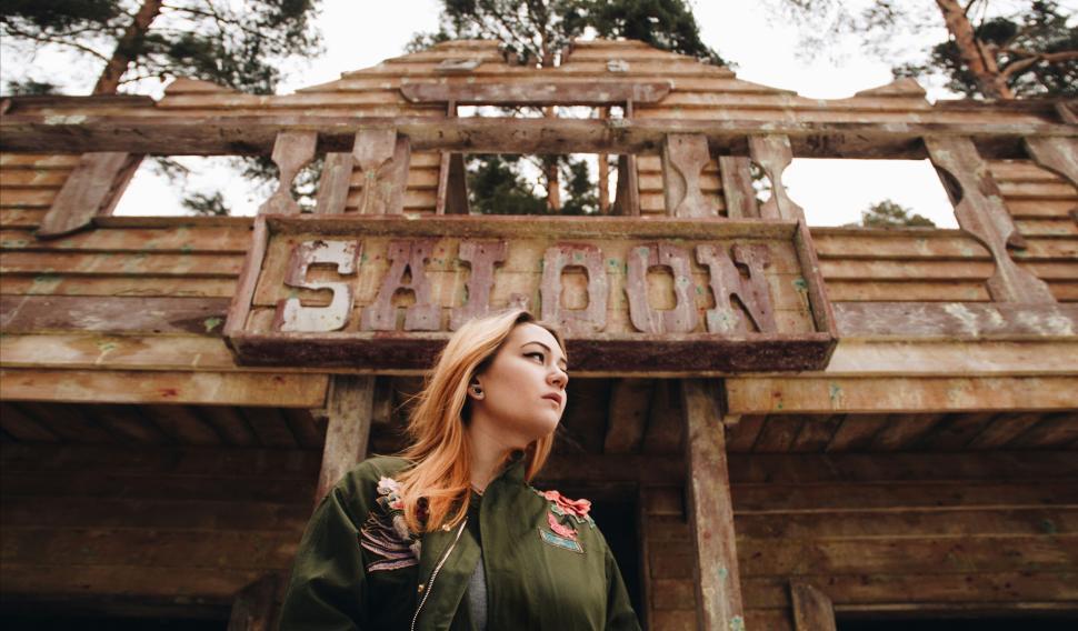 Free Image of Young woman in front of a rustic saloon building, looking away 