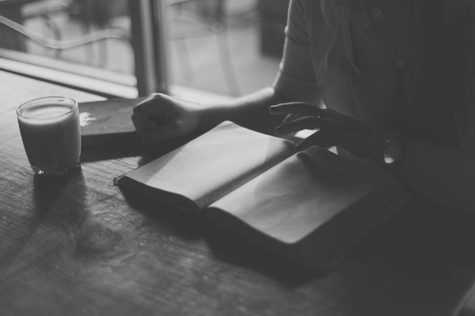 Free Image of Person reading a book with a cup of coffee on wooden table nearby. 