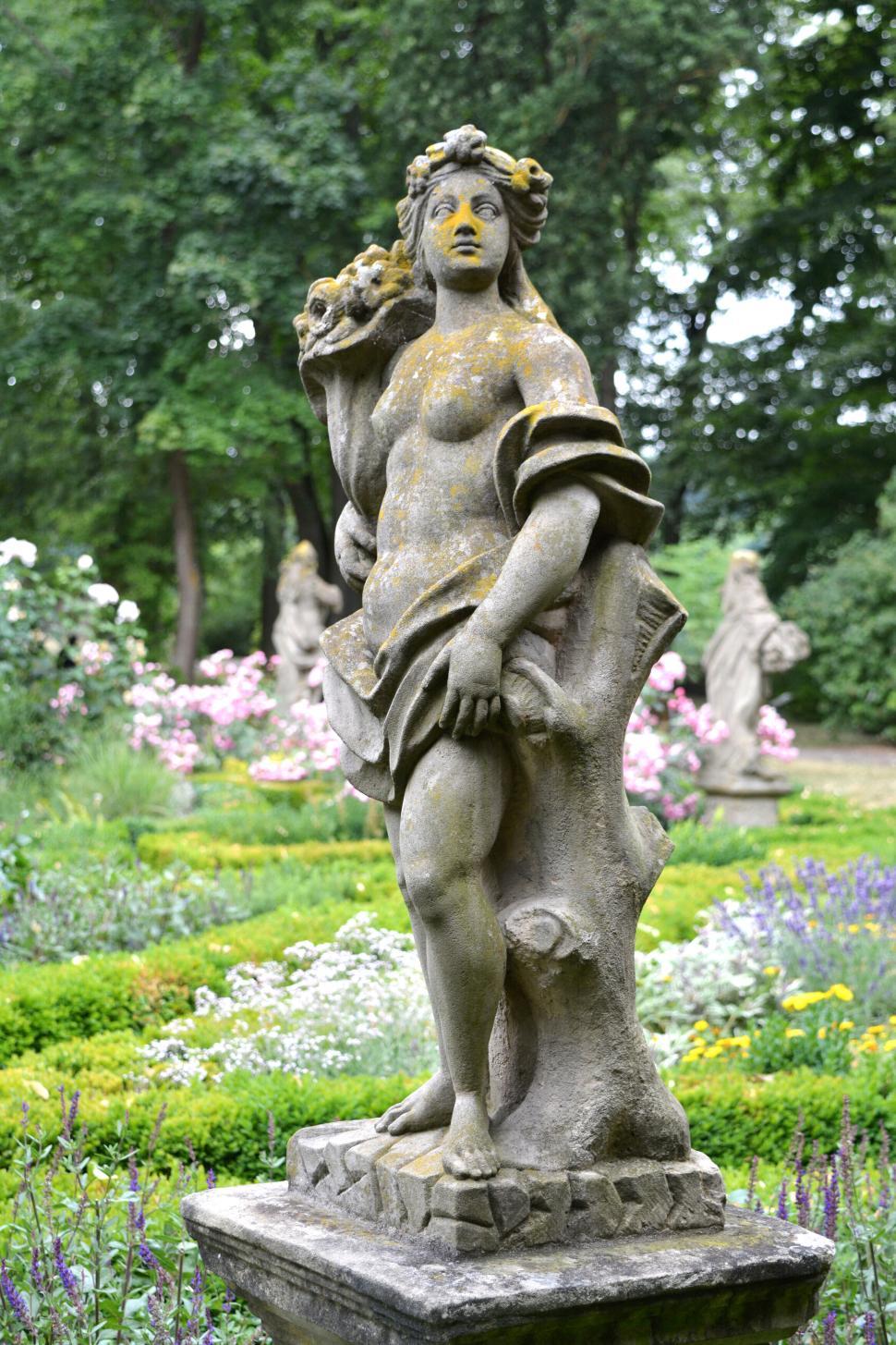 Free Image of Stone statue of a woman holding flowers in a lush garden 