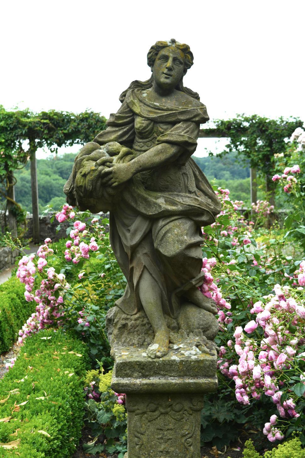 Free Image of Stone statue of a woman holding a basket in a lush flower garden 