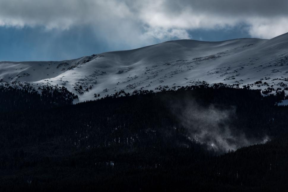 Free Image of Snow-capped mountains under cloudy sky with forest below 