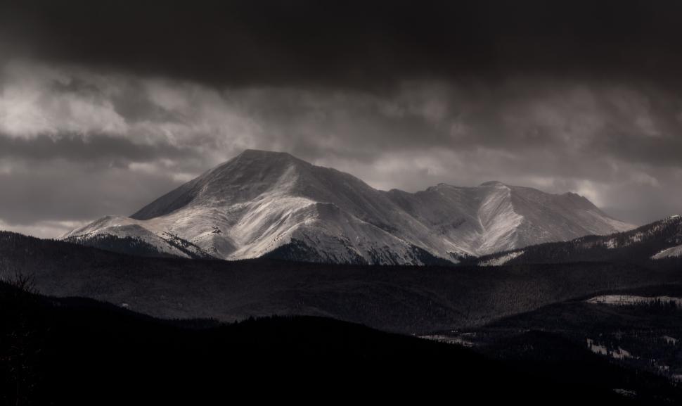 Free Image of Snow-covered mountains under a dark cloudy sky 