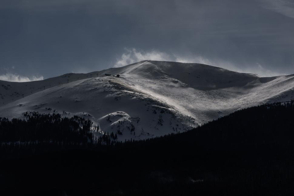 Free Image of Snow-covered mountain and dark forest under cloudy sky 