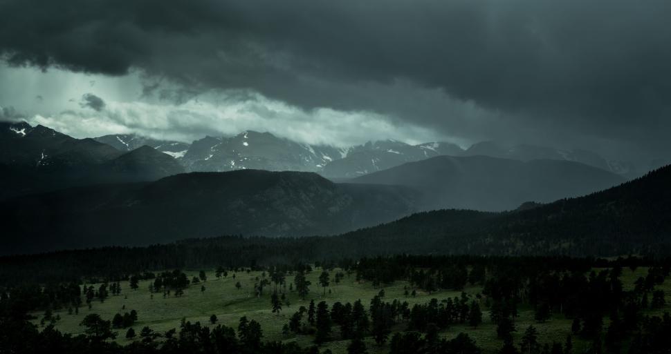 Free Image of Stormy mountain range looms over green valley under mist 