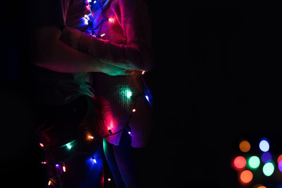 Free Image of Romantic couple wrapped in colorful fairy lights embrace 